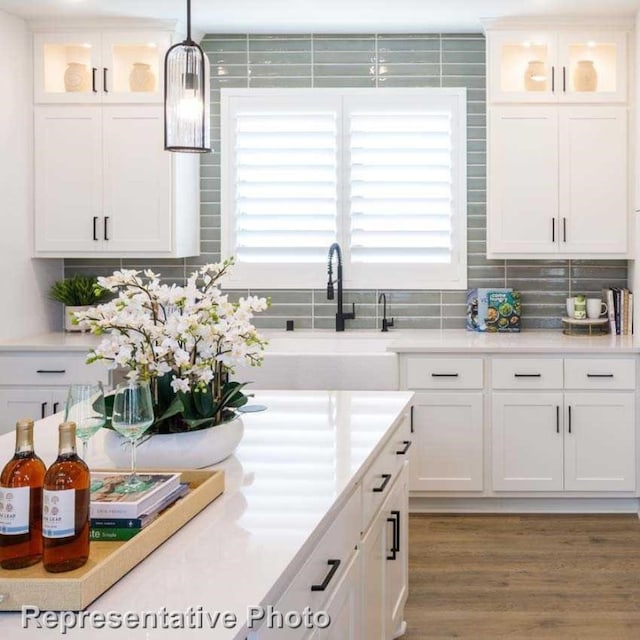 kitchen with tasteful backsplash, sink, wood-type flooring, white cabinetry, and hanging light fixtures