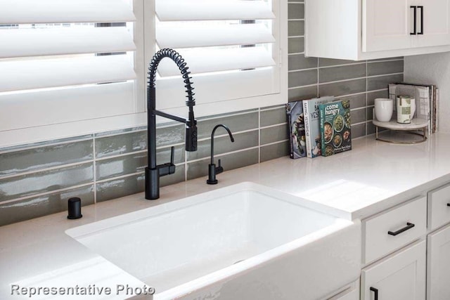 interior details featuring decorative backsplash, white cabinetry, and sink