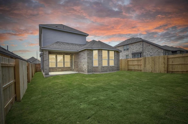 rear view of house with a fenced backyard, a patio, a yard, and brick siding