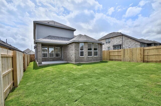 rear view of house with a fenced backyard, a patio, a lawn, and brick siding
