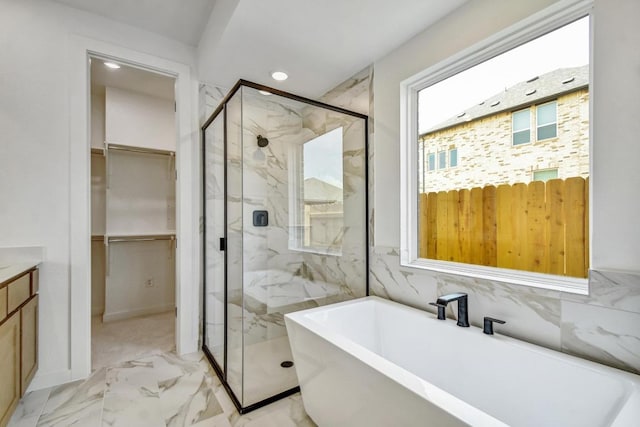 bathroom with marble finish floor, a walk in closet, recessed lighting, a soaking tub, and a marble finish shower