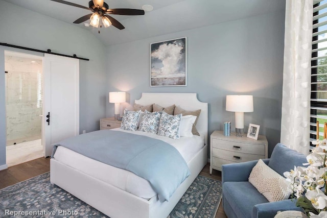 bedroom featuring ensuite bath, ceiling fan, dark wood-type flooring, a barn door, and lofted ceiling