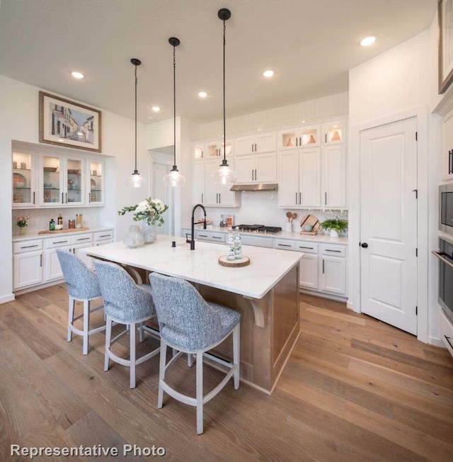 kitchen featuring a center island with sink, wood-type flooring, white cabinetry, and stainless steel appliances