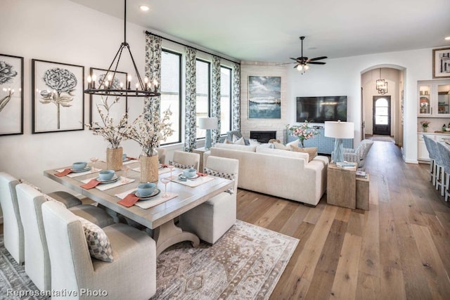 dining space with a fireplace, wood-type flooring, and ceiling fan with notable chandelier