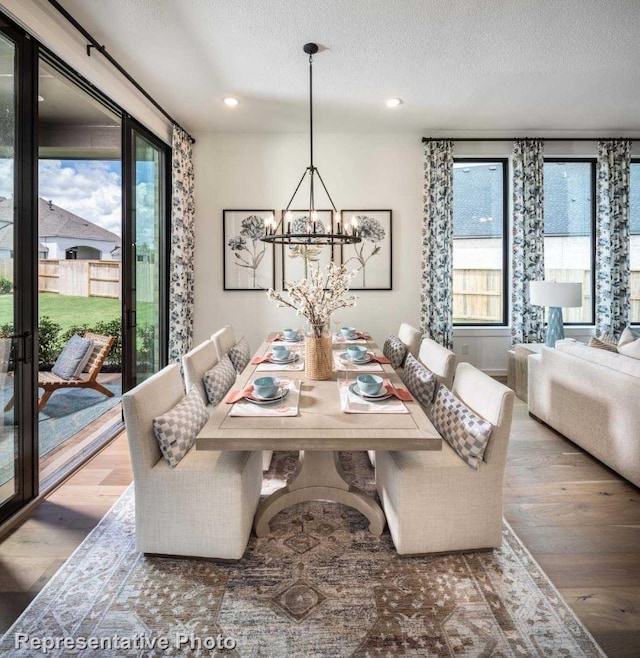 dining area with hardwood / wood-style flooring, a healthy amount of sunlight, a textured ceiling, and an inviting chandelier