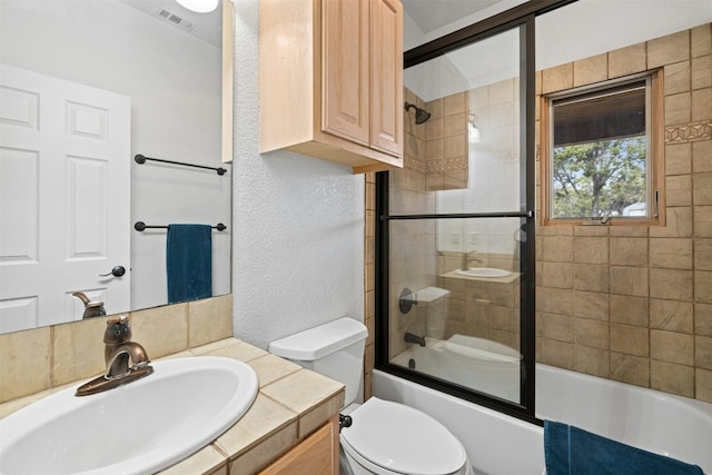 full bathroom featuring vanity, bath / shower combo with glass door, and toilet