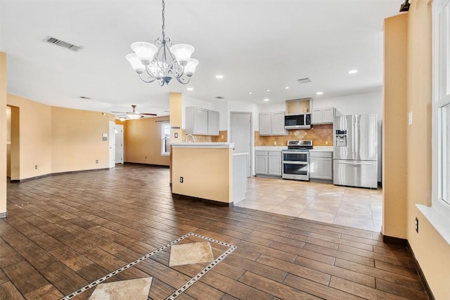 kitchen featuring appliances with stainless steel finishes, tasteful backsplash, ceiling fan with notable chandelier, white cabinetry, and hanging light fixtures