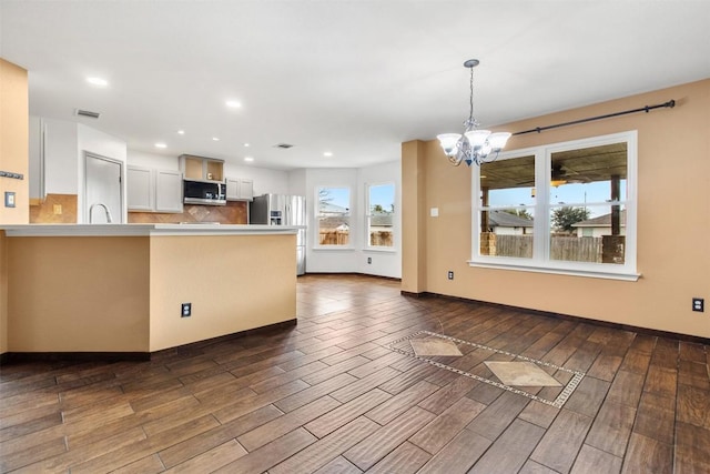 kitchen featuring kitchen peninsula, appliances with stainless steel finishes, backsplash, a chandelier, and white cabinetry