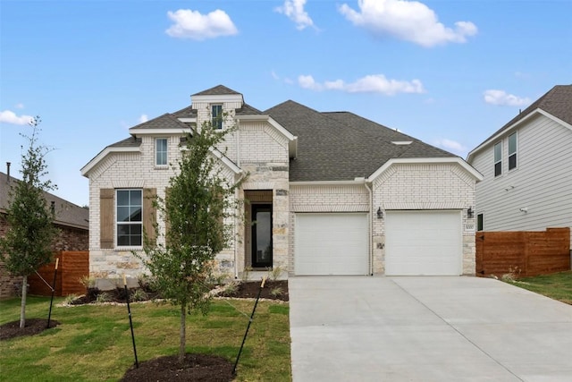 french country home featuring concrete driveway, roof with shingles, fence, and a garage