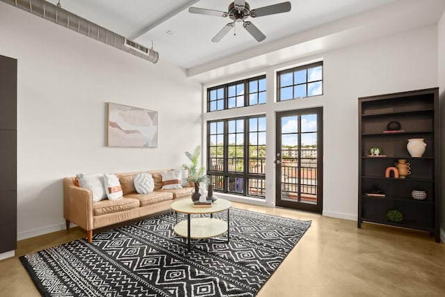 living room with finished concrete flooring, a towering ceiling, a ceiling fan, and baseboards