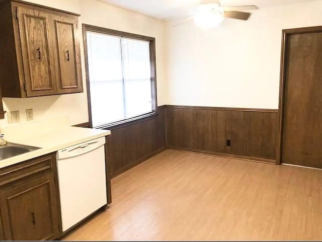 kitchen with ceiling fan, wooden walls, sink, light hardwood / wood-style flooring, and dishwasher