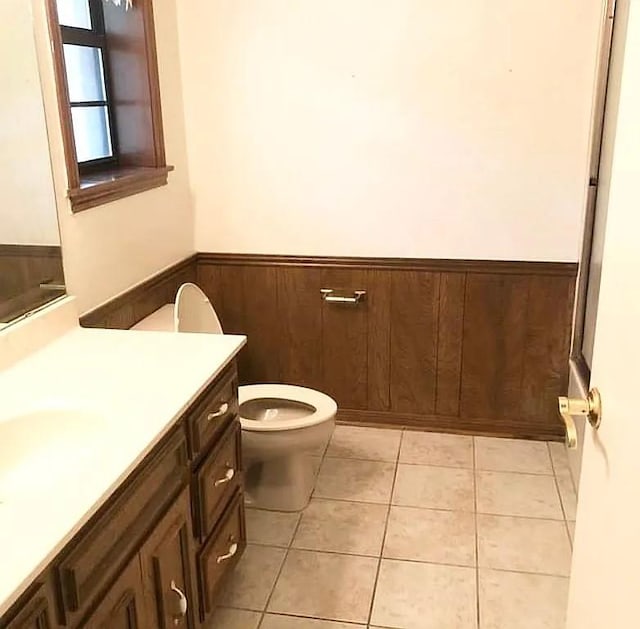 bathroom with wooden walls, tile patterned flooring, vanity, and toilet