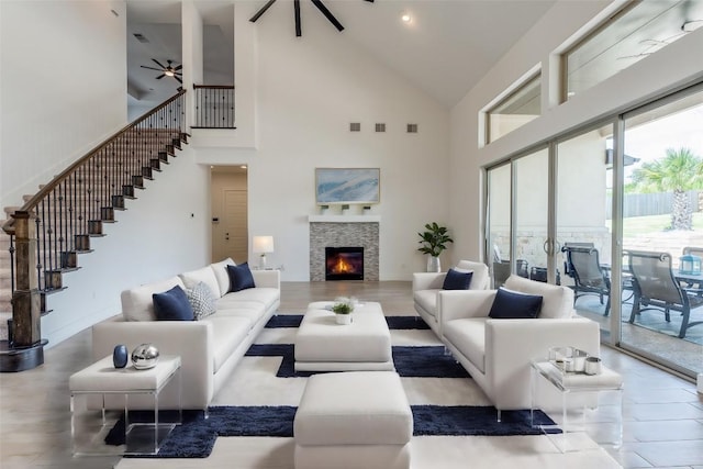 living room featuring ceiling fan, a stone fireplace, and a towering ceiling