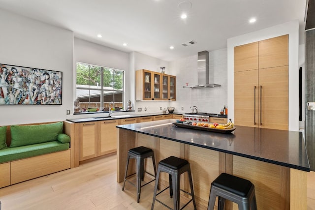 1005 Jewell St, Austin, TX 78704 - kitchen with wall chimney exhaust hood, a kitchen breakfast bar, tasteful backsplash, glass insert cabinets, and light wood-type flooring