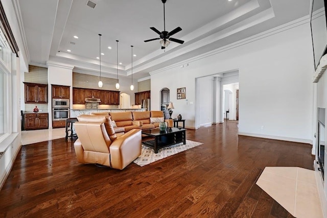 living room with a tray ceiling, dark hardwood / wood-style floors, crown molding, and ceiling fan