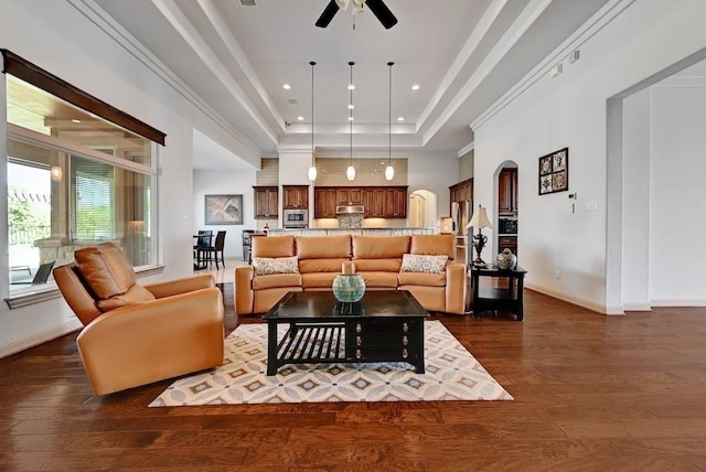 living room featuring a tray ceiling, dark hardwood / wood-style floors, ornamental molding, and ceiling fan