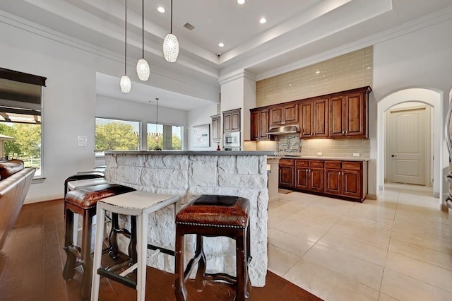 kitchen featuring a kitchen breakfast bar, stainless steel appliances, hanging light fixtures, and a tray ceiling