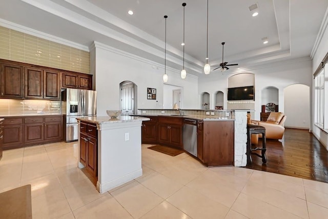 kitchen with a tray ceiling, stainless steel appliances, pendant lighting, a center island with sink, and light tile patterned flooring