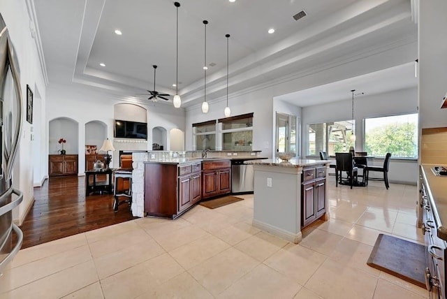 kitchen with a raised ceiling, a center island with sink, light tile patterned flooring, and stainless steel appliances