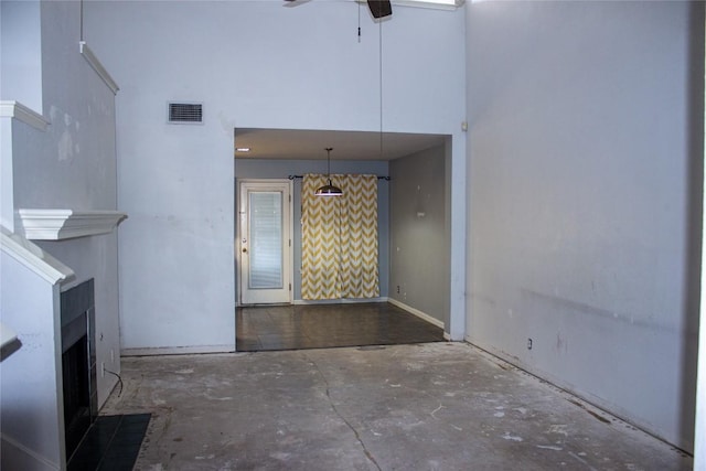 unfurnished living room featuring ceiling fan, a towering ceiling, and concrete flooring