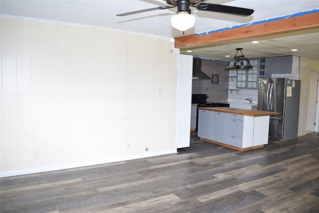 kitchen with wall chimney range hood, dark hardwood / wood-style floors, stainless steel fridge, beamed ceiling, and butcher block counters