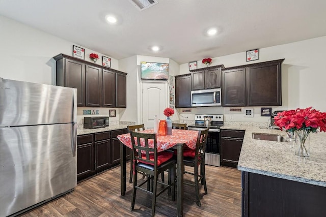 kitchen with light stone countertops, dark brown cabinetry, dark hardwood / wood-style flooring, stainless steel appliances, and sink