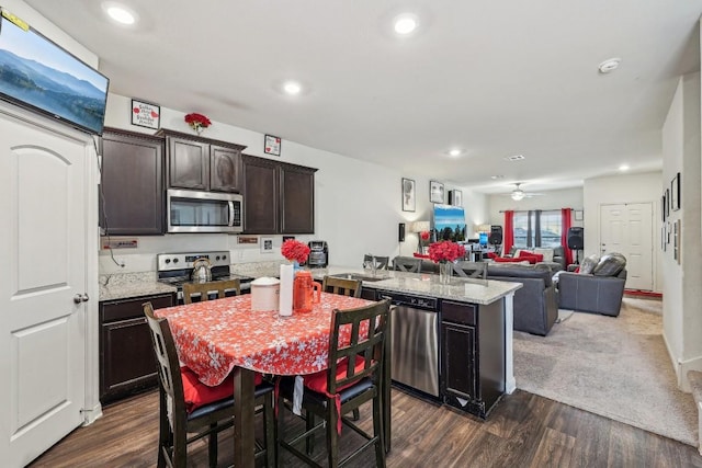 kitchen featuring light stone countertops, dark brown cabinetry, appliances with stainless steel finishes, dark wood-type flooring, and ceiling fan