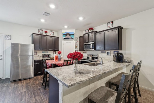 kitchen with kitchen peninsula, sink, a kitchen breakfast bar, stainless steel appliances, and dark brown cabinets