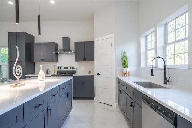 kitchen featuring tasteful backsplash, wall chimney exhaust hood, stainless steel appliances, sink, and hanging light fixtures