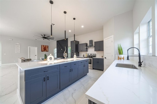 kitchen with stainless steel range with electric stovetop, pendant lighting, wall chimney range hood, sink, and an island with sink