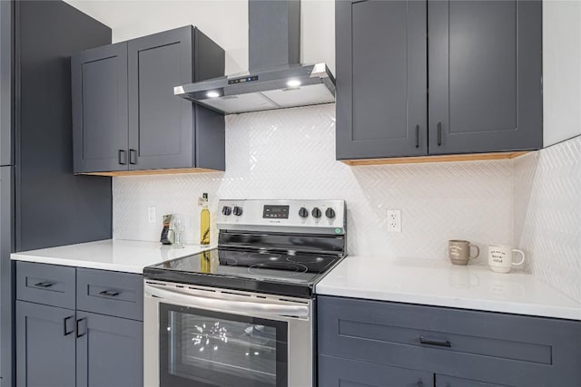 kitchen with gray cabinetry, wall chimney exhaust hood, decorative backsplash, and stainless steel electric range oven