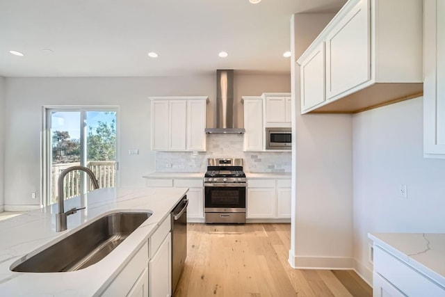 kitchen featuring light stone counters, stainless steel appliances, wall chimney range hood, white cabinets, and sink