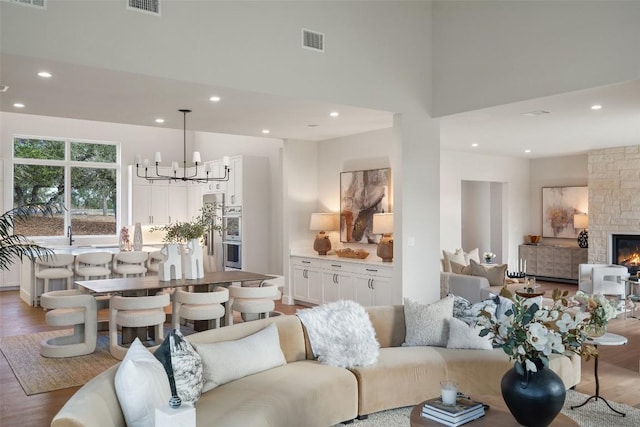 living room featuring hardwood / wood-style floors, a stone fireplace, a notable chandelier, and a high ceiling