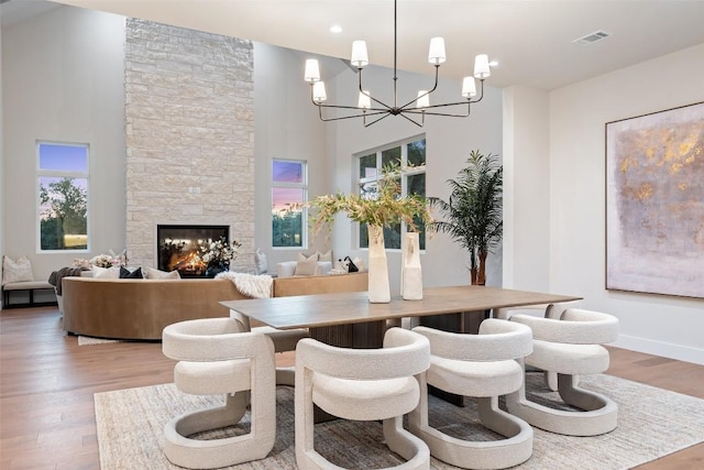 dining area with wood-type flooring, a towering ceiling, a fireplace, and a chandelier