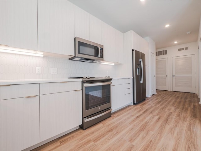 kitchen featuring decorative backsplash, white cabinets, stainless steel appliances, and light wood-type flooring