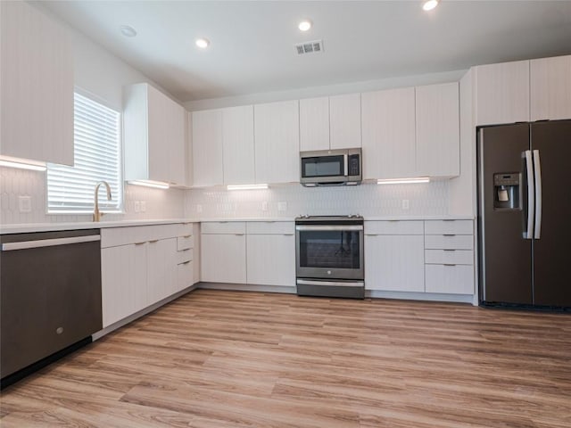 kitchen with white cabinets, light wood-type flooring, stainless steel appliances, and tasteful backsplash