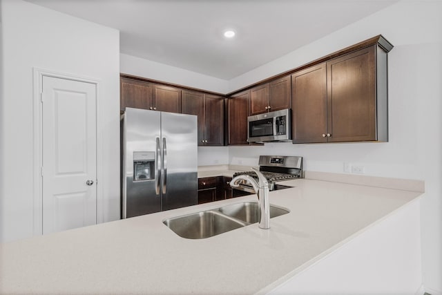 kitchen featuring kitchen peninsula, stainless steel appliances, dark brown cabinets, and sink