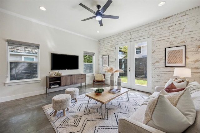 living room with french doors, wooden walls, ceiling fan, ornamental molding, and concrete flooring