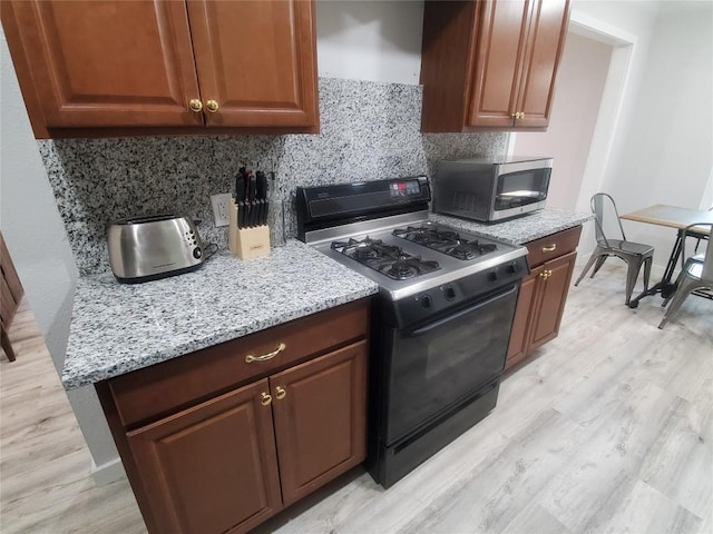 kitchen with gas stove, light stone countertops, tasteful backsplash, and light hardwood / wood-style floors