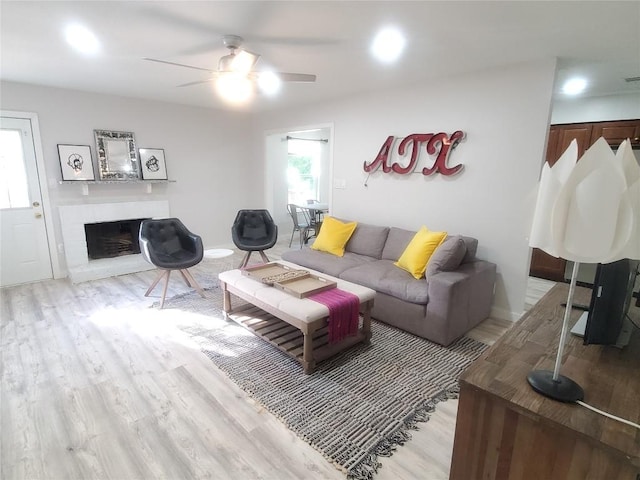 living room featuring ceiling fan, light hardwood / wood-style flooring, and a brick fireplace