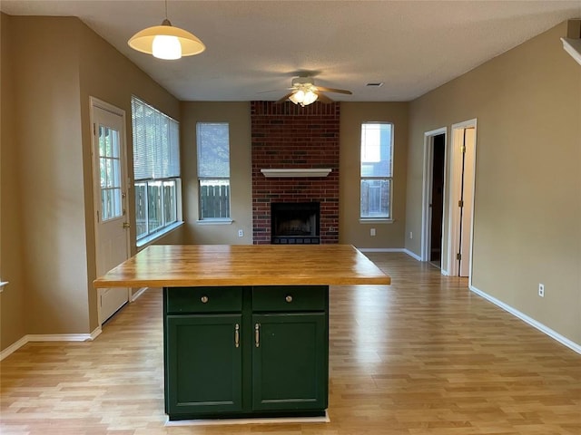 kitchen with a center island, a brick fireplace, green cabinets, butcher block countertops, and pendant lighting