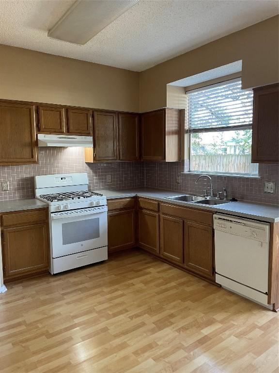 kitchen with a textured ceiling, sink, white appliances, and light hardwood / wood-style flooring