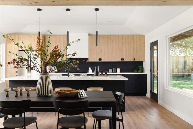 kitchen featuring a center island, hanging light fixtures, light wood-type flooring, light brown cabinetry, and tasteful backsplash