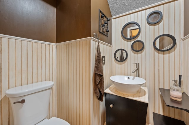 bathroom with wooden walls, vanity, vaulted ceiling, and toilet