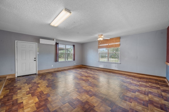 empty room with an AC wall unit, dark parquet flooring, ceiling fan, and a textured ceiling