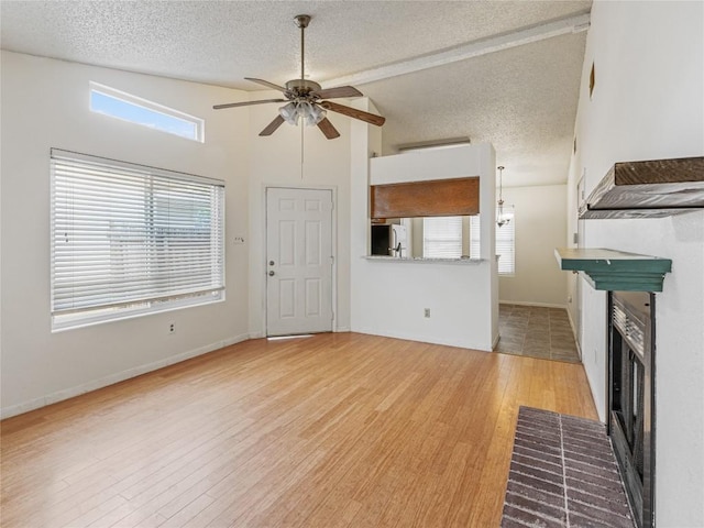 unfurnished living room featuring a textured ceiling, ceiling fan, lofted ceiling, and a brick fireplace