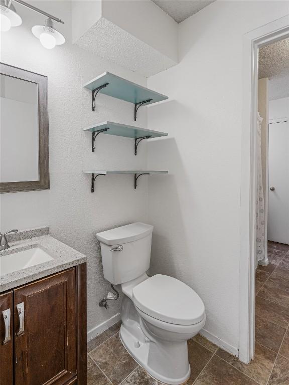 bathroom with a textured ceiling, vanity, and toilet