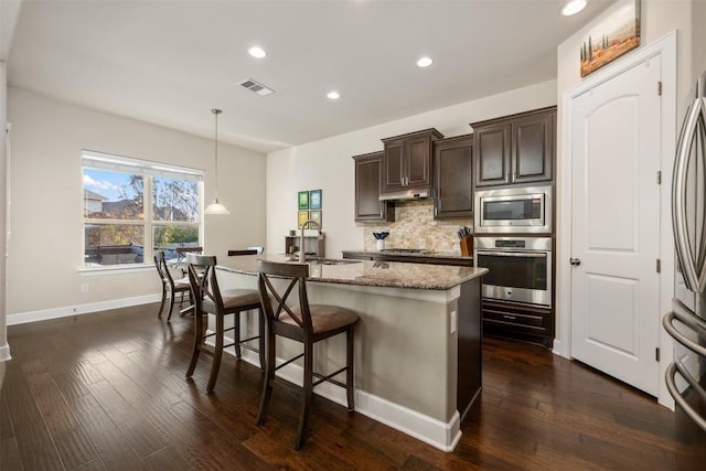 2715 Mariposa Way, Round Rock, TX 78665 - kitchen with stainless steel appliances, dark brown cabinets, light stone counters, backsplash, and an island with sink