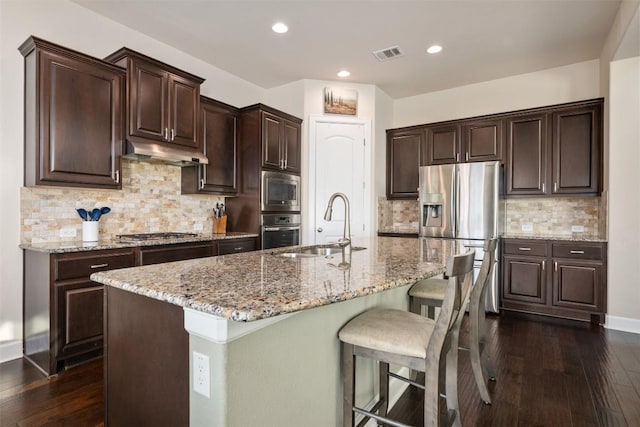 kitchen featuring a center island with sink, dark brown cabinetry, sink, and appliances with stainless steel finishes