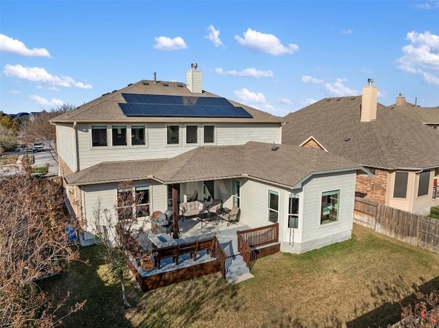 rear view of house featuring a shingled roof, fence, roof mounted solar panels, a chimney, and a yard